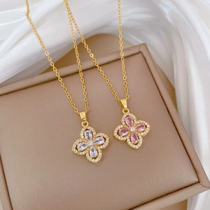 Detailed close-up of two clover necklaces in gold with white and pink crystal pendants