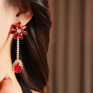 Detailed close-up of long gold drop earrings with red flower design and pear-cut gemstone