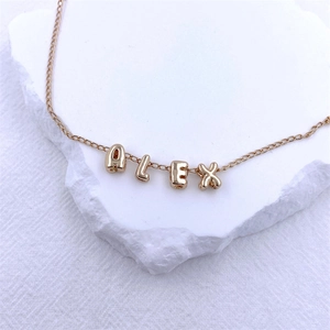 Detailed shot of golden KC bubble alphabet charms spelling ALEX on white stone