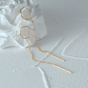 Detailed shot of golden tassel drop earrings hanging on a minimalist white sculpture
