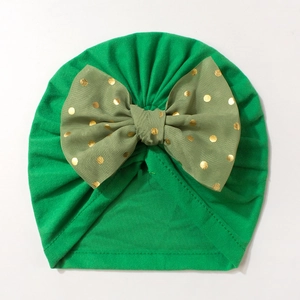 Detail of baby turban hat featuring a large gold polka dot olive green bow on soft fabric