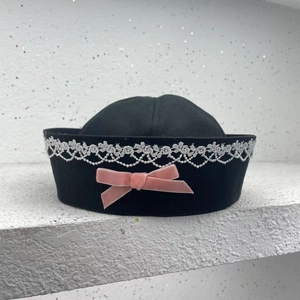 Detail of black sailor hat featuring white lace trim and a pink velvet bow decoration