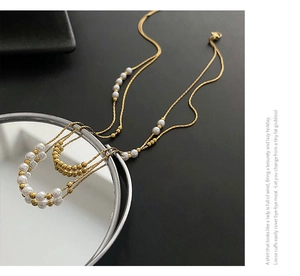Detail view of a double-layered titanium steel necklace with elegant white pearls and gold beads