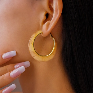 Close-up of a C-shaped amber acetate hoop earring with golden metal inner trim on a model