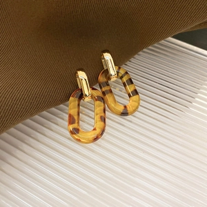 Macro shot of gold metal buckle and amber leopard print acrylic oval drop earrings