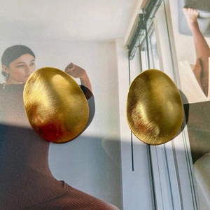 Minimalist large oval earrings with gold brushed finish on fashion magazine background