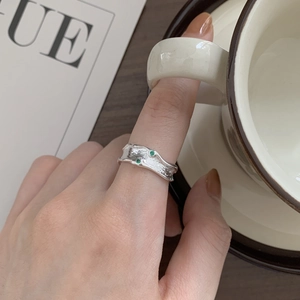 Minimalist silver S925 irregular ring with green stones worn by hand with a ceramic cup