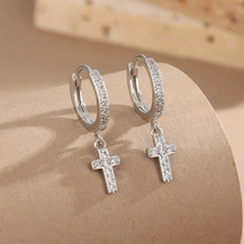 Macro shot of silver cross hoop earrings with white zircon stones on a warm textured base