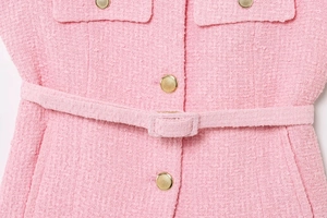 Detail of pink tweed dress showing golden embossed buttons and a matching waist belt