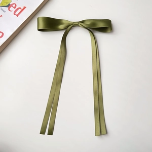 Detail of elegant dark green satin ribbon bow hair clip with smooth glossy silk texture