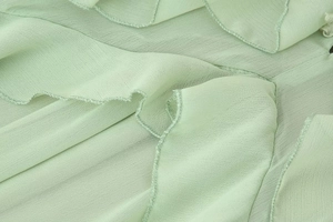 Detailaufnahme von hellgrünem Chiffonstoff mit gestuften Rüschen und plissierter Textur