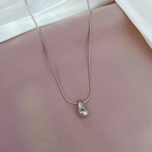 Detailed view of silver water drop pendant on a sleek snake chain over silk fabric