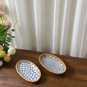 Detail of oval ceramic snack trays with blue floral patterns and hand-woven rattan edges