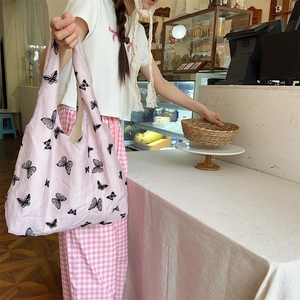 Lifestyle shot of pink lace tote bag featuring black butterfly prints in a cafe setting