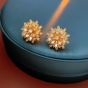 Macro detail of gold-plated flower stud earrings featuring sparkling white zircon stones