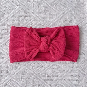 Detailed close-up of dark pink cable-knit nylon baby headband with large bow detail