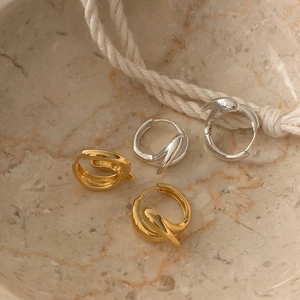 Detailed view of twisted crossover hoop earrings in gold and silver finish on marble