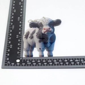 Flat lay of realistic acrylic cow pendant with silver bead chain and measuring scale