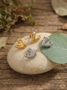 Detailed close-up of textured heart stud earrings in gold and silver on natural stones