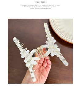 Detail of transparent floral hair claw clip featuring small white flowers and gold spring