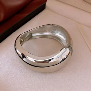 Polished silver irregular wide metal bangle with hinge on a beige jewelry display box