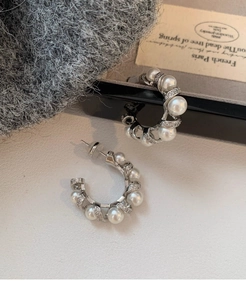 Close-up of elegant C-shaped silver earrings with spiral pearls and tiny crystals