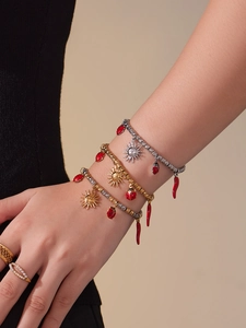 Detail of layered gold bracelets with sun charms, ladybug pendants and a chili horn accessory