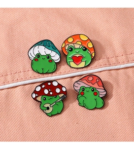 Detailed view of four colorful enamel frog mushroom pins on a pink fabric background