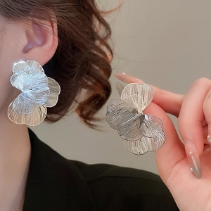 Gros plan de boucles d'oreilles fleurs argentées montrant la texture du métal brossé