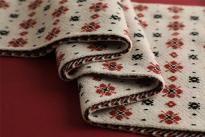 Close-up of beige knitted Christmas scarf featuring red and black geometric floral patterns