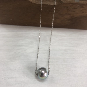 Close-up of a dark grey pearl pendant on a silver s925 chain over a wood block