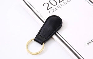 Close-up of black PU leather keychain with gold metal ring on a minimalist calendar