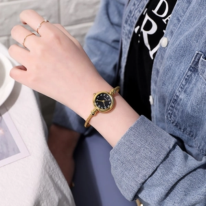 Detail of a lady's golden rope bracelet watch with a minimalist black dial on a wrist