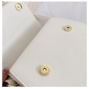 Detailed view of the fine leather texture and golden magnetic buckle on white crossbody bag