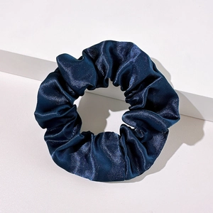 Detail of a dark blue satin scrunchie with silky texture on a white geometric stand