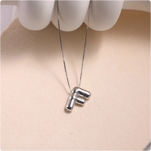 Macro shot of silver letter F balloon-style pendant with a smooth mirror finish