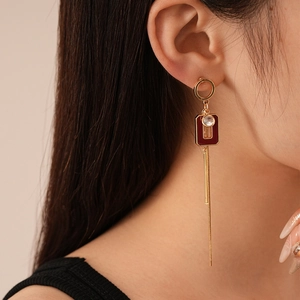 Detail of long gold tassel earrings with red geometric pendant and sparkling diamond accents