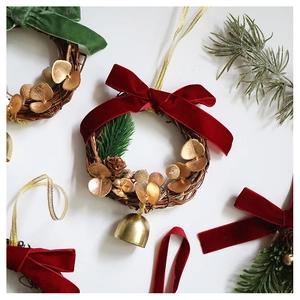 Detail of Christmas wreath with velvet bow, brass bell, and golden leaves on white backdrop