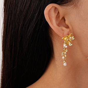 Detail of elegant gold flower and leaf earrings with pearls worn by a model