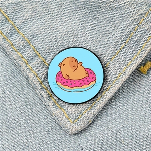 Cute capybara enamel pin on pink donut floatie attached to blue denim jacket fabric