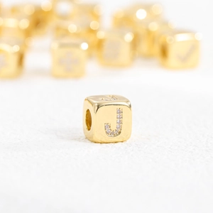 Macro shot of gold cube pendant with cubic zirconia letter J and polished metal finish