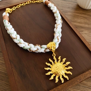 Detailed macro view of bohemian woven cotton rope necklace with a hammered gold sun pendant