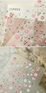 Detail of 3D embossed nail stickers featuring red roses, daisies, and golden moon stars