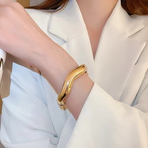Detailed view of polished gold wavy bangle on wrist showing mirror finish and fluid lines