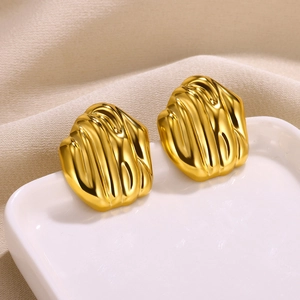Macro shot of gold-tone textured petal earrings on white ceramic and yellow silk