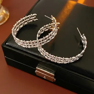 Silver wide-band C-shaped hoop earrings with woven chain texture on black leather background
