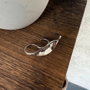 Artistic leaf design silver ring on dark wood surface with ceramic detail