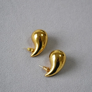 Detail shot of high-polish gold teardrop earrings with minimalist metallic texture