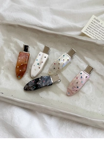Detail of five teardrop rhinestone hair clips with marble textures on a ceramic tray
