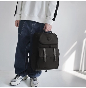 Detail of black flap backpack with buckle pockets shown on model for casual street style